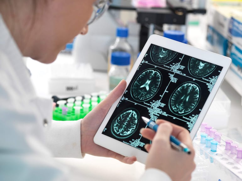 Científica en bata blanca analiza resonancias magnéticas en su tablet, sosteniendo un bolígrafo en la mano derecha en un laboratorio.
