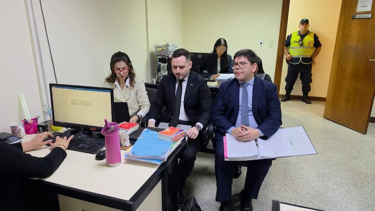 Silvio Corbeta y Jorge Luis Arce Rolandi en trajes oscuros, Marlene González trabaja en computadora con expresión concentrada.