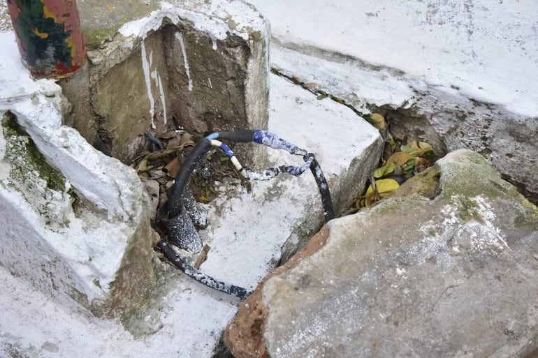Espacio deteriorado en plaza con postes desgastados y cables eléctricos expuestos, reflejando abandono. Sin personas presentes.