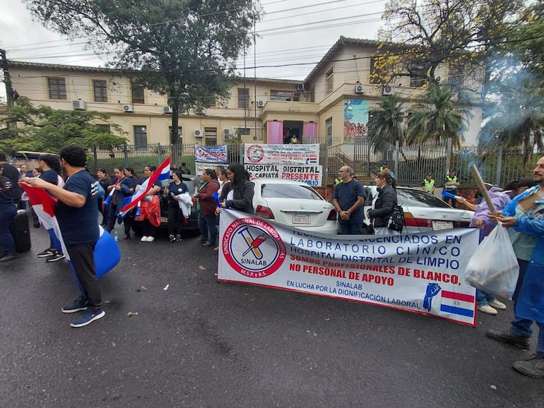 Grupo de laboratoristas con banderas y pancarta del sindicato Sinalab, en un clima nublado frente al hospital.