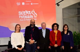 Seis músicos en el escenario, vestidos de negro, tocan violines y cello, mientras el público observa con teléfonos móviles.