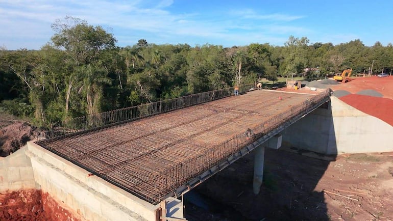 Varios trabajadores en el puente en construcción, rodeados de vegetación y maquinaria en un entorno natural.