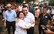 Luis Bello y José Gregorio Ledesma Narvaez abrazados, ambos sonrientes, rodeados de una multitud en un entorno urbano.