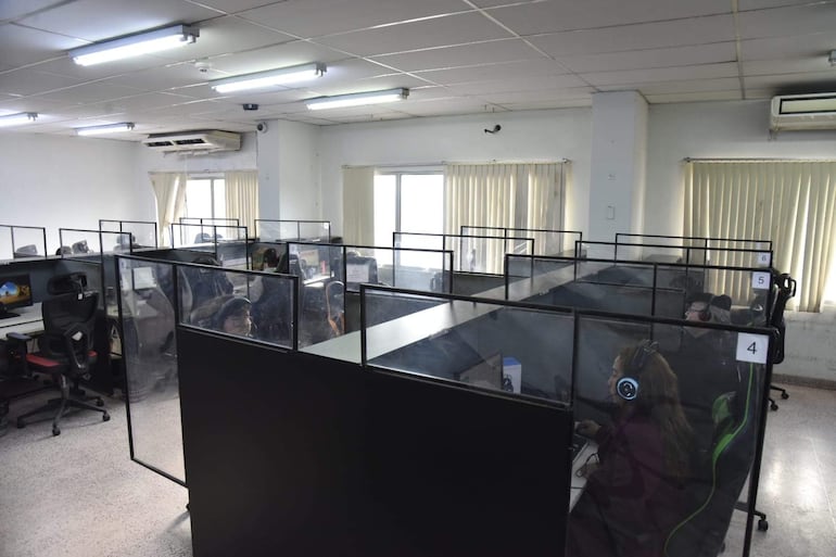 Diez empleados en call center del IPS, concentrados frente a computadoras, usando auriculares en ambiente iluminado.