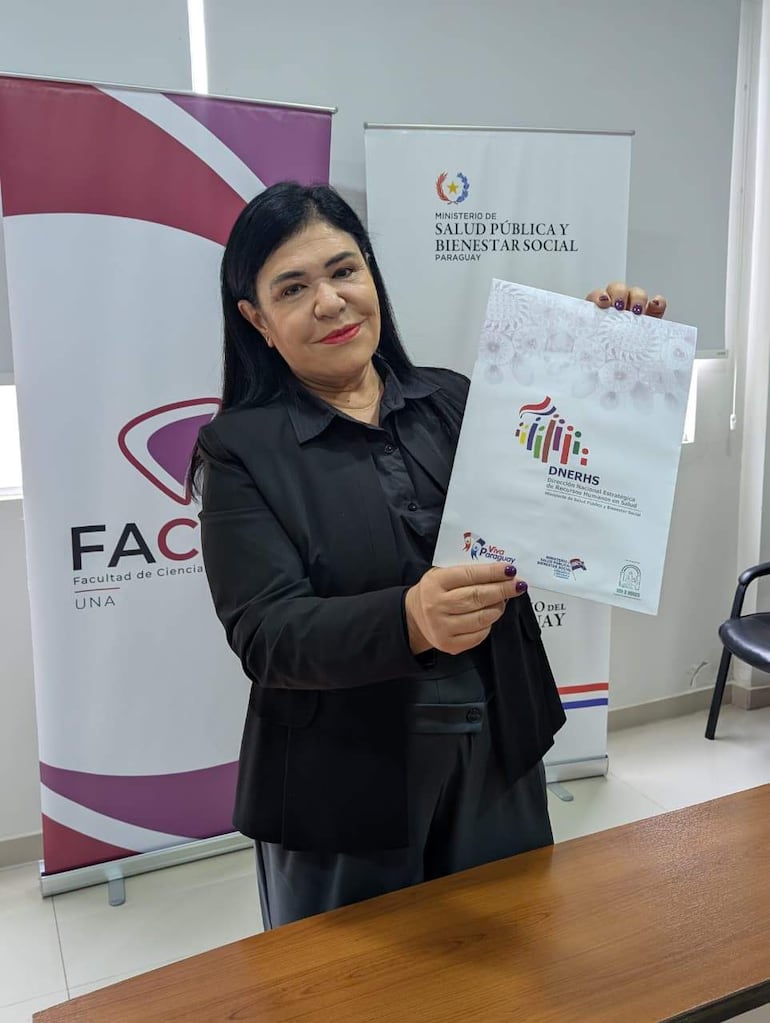 Mujer en camisa negra y chaqueta sostiene un documento, detrás hay banners de FAC y MSP y BS en un ambiente institucional.