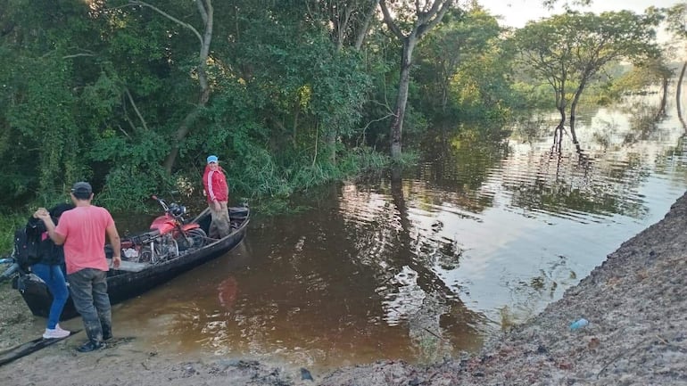 Hombre en canoa con camiseta roja, otro en camiseta rosa ayuda a una mujer con mochila negra en orilla.