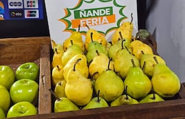Exhibición de peras en recipiente de madera, con variedad de colores, y cartel de ofertas sin personas presentes.