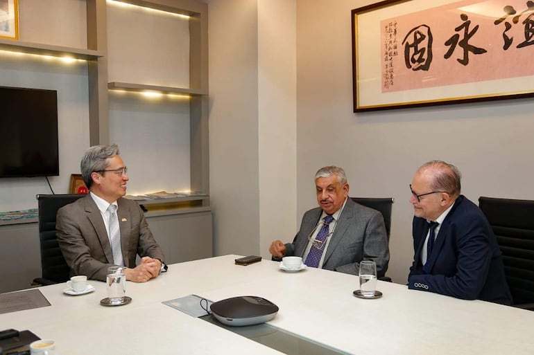 Isaías Fretes de cabello canoso y gafas, Iván Lee con cabello claro y serio, conversando en una oficina moderna.