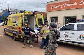 Grupo de personas ayuda a un rehén en camilla mientras un bombero y un policía observan la situación en un entorno urbano.