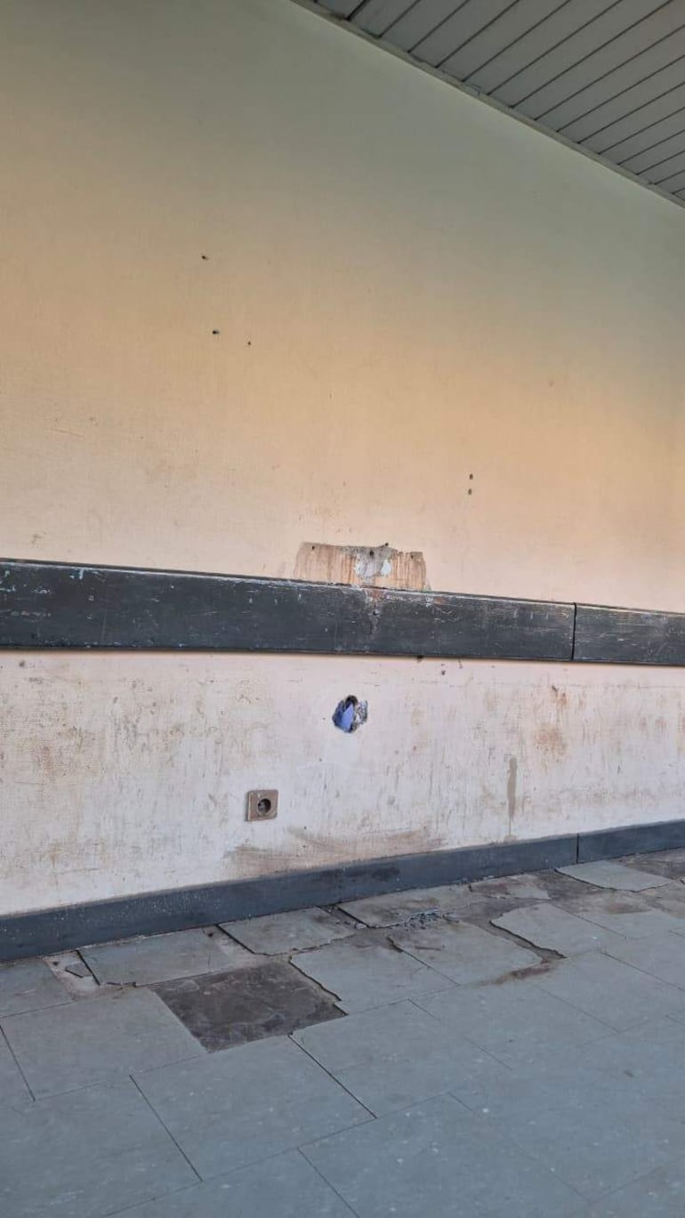Pared desgastada de hospital con marcas visibles y baldosas de colores, sin personas presentes.