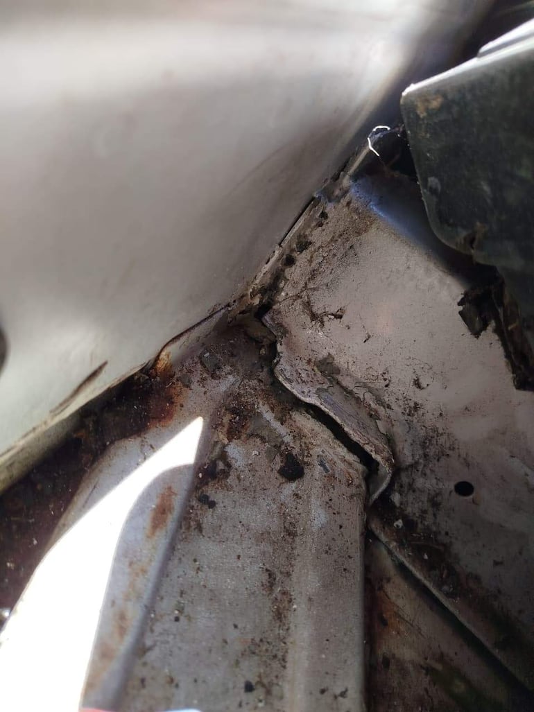 Primer plano de un chasis metálico deteriorado con manchas de óxido y daños visibles, sin personas en el entorno.