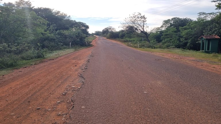 Carretera de tierra poco transitada rodeada de vegetación densa, con un pequeño refugio verde al lado derecho.