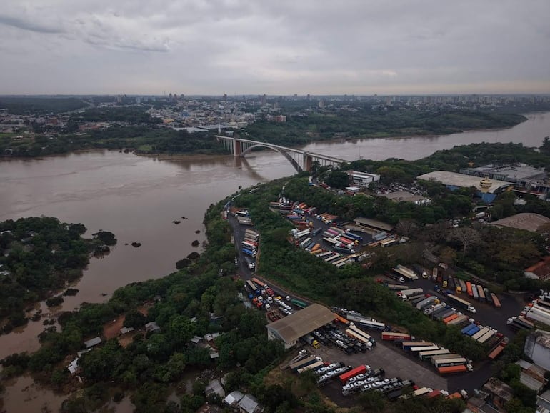 Panorama del barrio San Rafael, con un río, puente y camiones en un área de carga, bajo un cielo nublado.