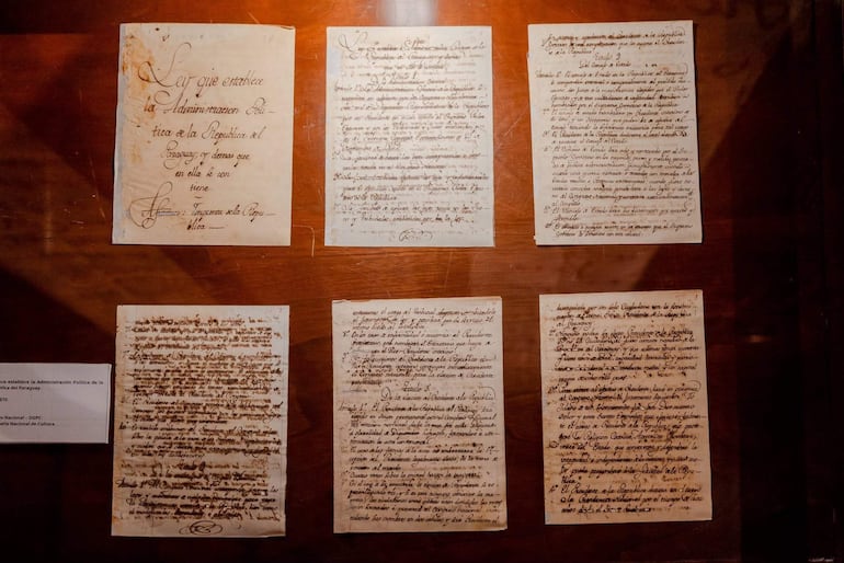 Documentos antiguos expuestos en un museo, dispuestos sobre una mesa de madera en ambiente oscuro.