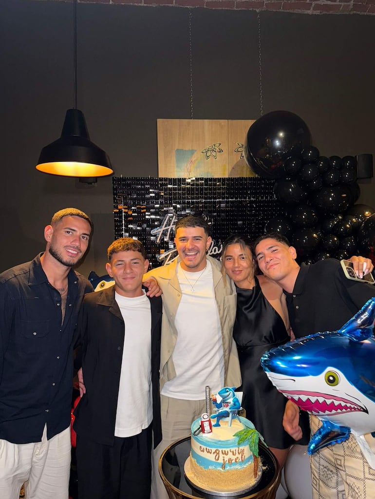 Antonio Sanabria sonríe con figura decorativa junto a un pastel, mientras sus cuatro amigos lo rodean en una fiesta decorada con globos.
