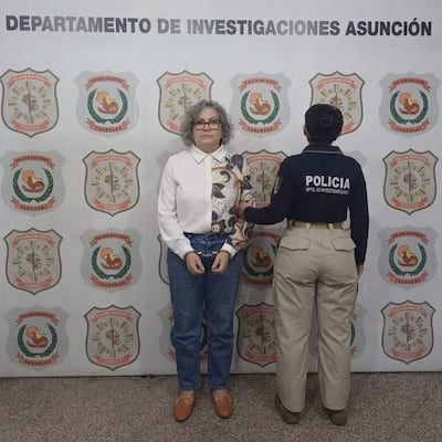 Rosa Colmán, de cabello rizado y canoso, vestida con camisa blanca y jeans, es sostenida por una mujer policía.