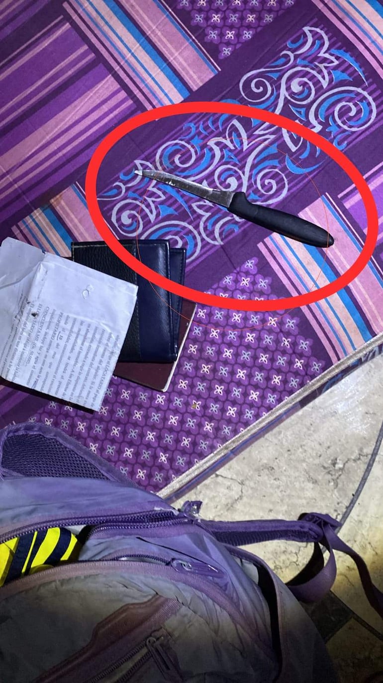 Cuchillo sobre tapete morado, documentos y mochila abiertos en un interior sin personas presentes.