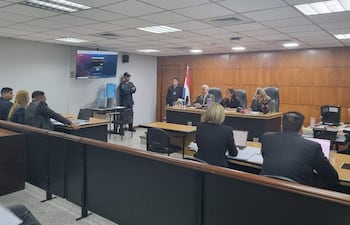 Cuatro personas detrás de una mesa en el tribunal, con un oficial de seguridad observando la escena desde el fondo.