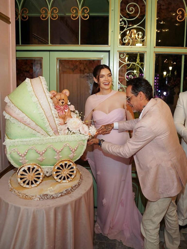 Nadia Ferreira sonríe con un vestido rosa claro mientras Marc Anthony sostiene un pastel decorado con un oso de peluche.