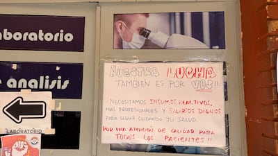 Cartel en puerta de laboratorio con texto que denuncia la falta de insumos y salarios dignos, fondo blanco y letras rojas y negras.