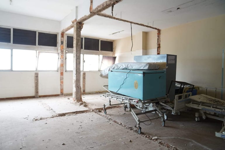 Interior del hospital en mal estado, con camas hospitalarias y escombros, revelando abandono y falta de mantenimiento.