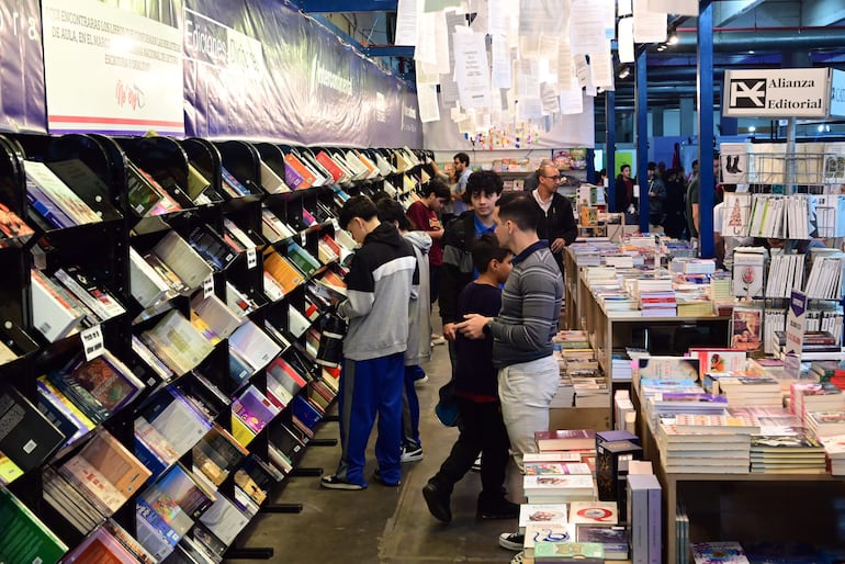 Grupo de jóvenes revisando libros en estantería en la FIL Asunción 2026, con ambiente acogedor y estantes llenos de publicaciones.