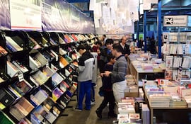 Grupo de jóvenes revisando libros en estantería en la FIL Asunción 2026, con ambiente acogedor y estantes llenos de publicaciones.