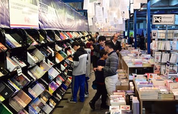 Grupo de jóvenes revisando libros en estantería en la FIL Asunción 2026, con ambiente acogedor y estantes llenos de publicaciones.