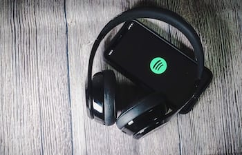 Auriculares negros sobre un teléfono móvil negro con logo de Spotify, en una superficie de madera, sin personas visibles.