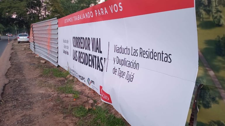 Valla publicitaria del Corredor Vial Las Residentas en un entorno urbano con vegetación y camino visible.