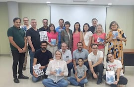 Grupo de personas sonrientes en ambiente interior, sosteniendo libros, con un niño al frente mirando hacia la cámara.