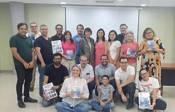 Grupo de personas sonrientes en ambiente interior, sosteniendo libros, con un niño al frente mirando hacia la cámara.