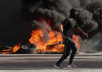Un palestino armado camina junto a un montón de neumáticos en llamas durante disturbios con tropas israelíes en el campo de refugiados en Jenin, Cisjordania.