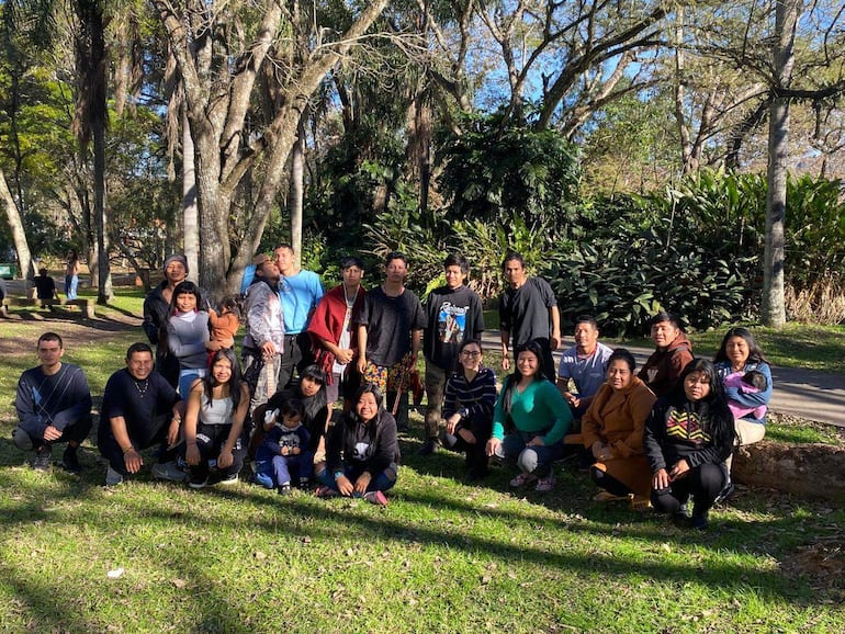 Grupo de aproximadamente 25 personas, incluyendo niños, en un parque, riendo y disfrutando del Día del Guaraní en un ambiente natural.