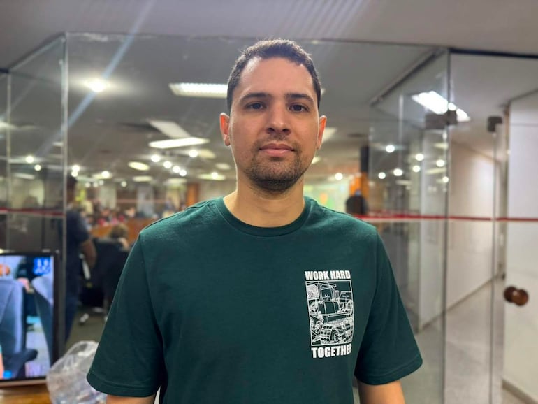 Pablo Callizo con camiseta verde que dice 'WORK HARD TOGETHER', de pie en un entorno de trabajo iluminado, con rostro tranquilo.