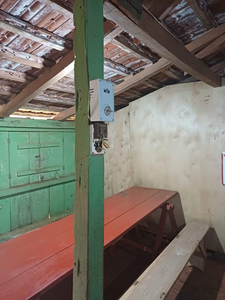 Interior de un comedor escolar con mesa roja y bancos de madera clara, sin personas visibles en la imagen.