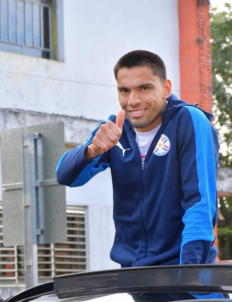 Diego Gómez sonriente en buzo azul, hace pulgar arriba, con un edificio urbano de fondo.