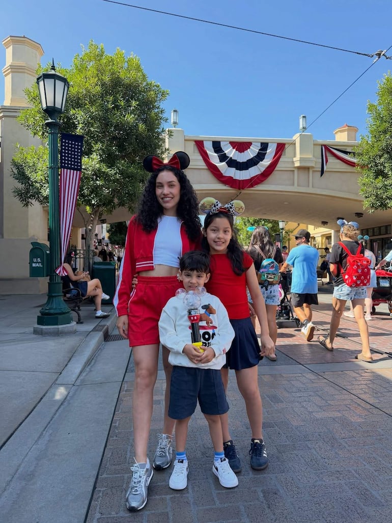 Dos niñas con orejas de Mickey y un niño sosteniendo un recipiente decorado, sonrientes en un ambiente festivo.