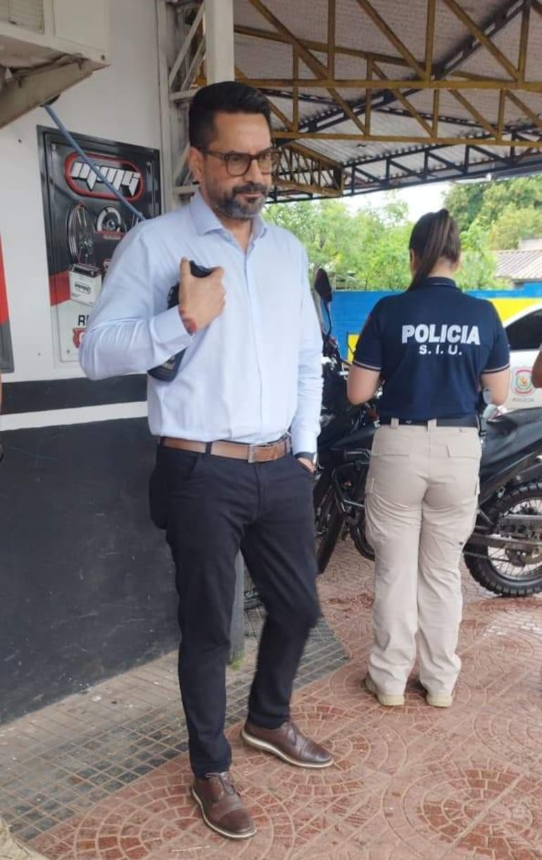 Gustavo Sandoval en camisa clara, atento, mientras una oficial de policía supervisa el área, con camiseta que dice 'POLICÍA'.