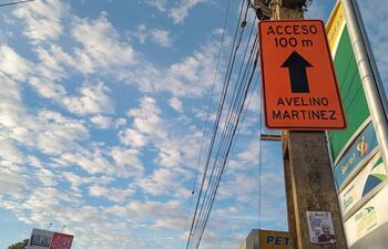 Cartel de tráfico naranja que señala 'ACCESO 100 m' en la Avenida Avelino Martínez rodeado de cables eléctricos.