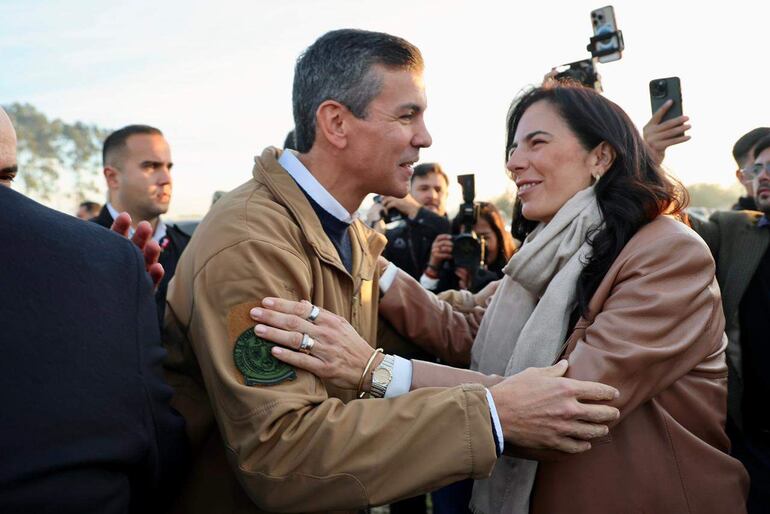 Dos mujeres sonrientes conversan durante la inauguración del CAIPI, una con abrigo beige y otra con chaqueta de cuero y bufanda clara.