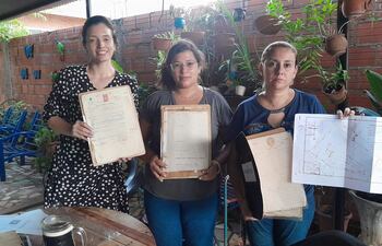 Larissa Ferreira, Cinthia Cáceres y Lourdes Sosa, hijas de los herederos de una propiedad de más de 9 hectáreas invadida en el 2000 en la zona de Pai Ñu Ñemby muestras los documentos originales que avalan la titularidad del terreno. Las mismas exigen desalojo, indemnización y pago por la parte expropiada por el estado en el 2019.