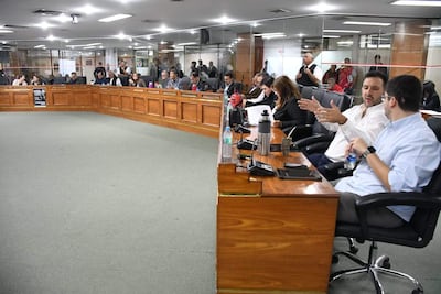 Cesar Escobar Ceres en camisa blanca y Miguel Sosa en camisa celeste dialogan en un ambiente formal, con documentos y dispositivos electrónicos.