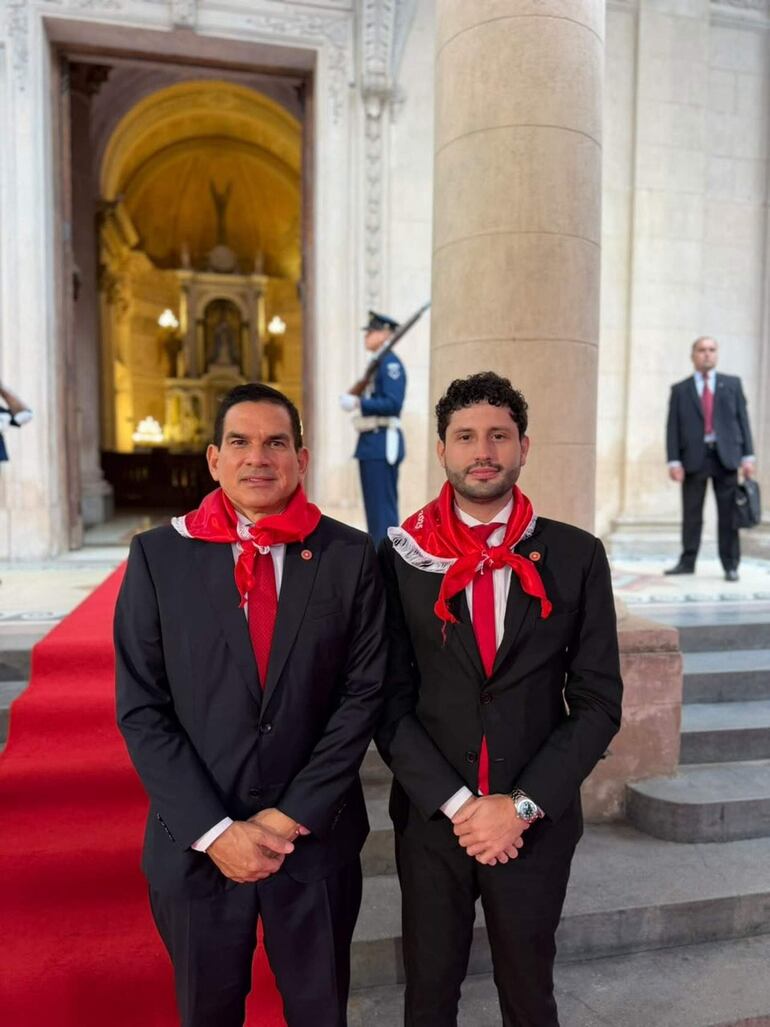 Dani Fernández con blazer y Juan Carlos Baruja en traje, ambos con expresiones tranquilas y bufanda, rodeados de personas.