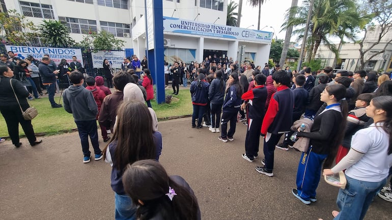 Estudiantes en ropa deportiva, mirando atentamente a un orador con micrófono en el evento de bienvenida.