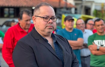 Óscar Pérez en chaqueta negra observa, mientras una multitud variada, con camisetas de diferentes colores, escucha atentos.