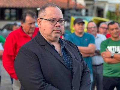 Óscar Pérez en chaqueta negra observa, mientras una multitud variada, con camisetas de diferentes colores, escucha atentos.