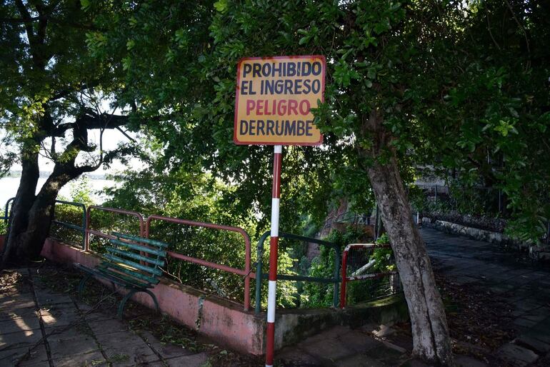 Letrero que dice 'PROHIBIDO EL INGRESO PELIGRO DERRUMBE' en un entorno natural con densa vegetación y un camino cubierto de hojas.
