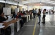 Un grupo de adultos, principalmente mujeres, se concentra en un taller electoral, mientras algunas completan formularios en mesas organizadas.