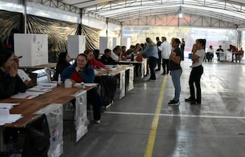 Un grupo de adultos, principalmente mujeres, se concentra en un taller electoral, mientras algunas completan formularios en mesas organizadas.